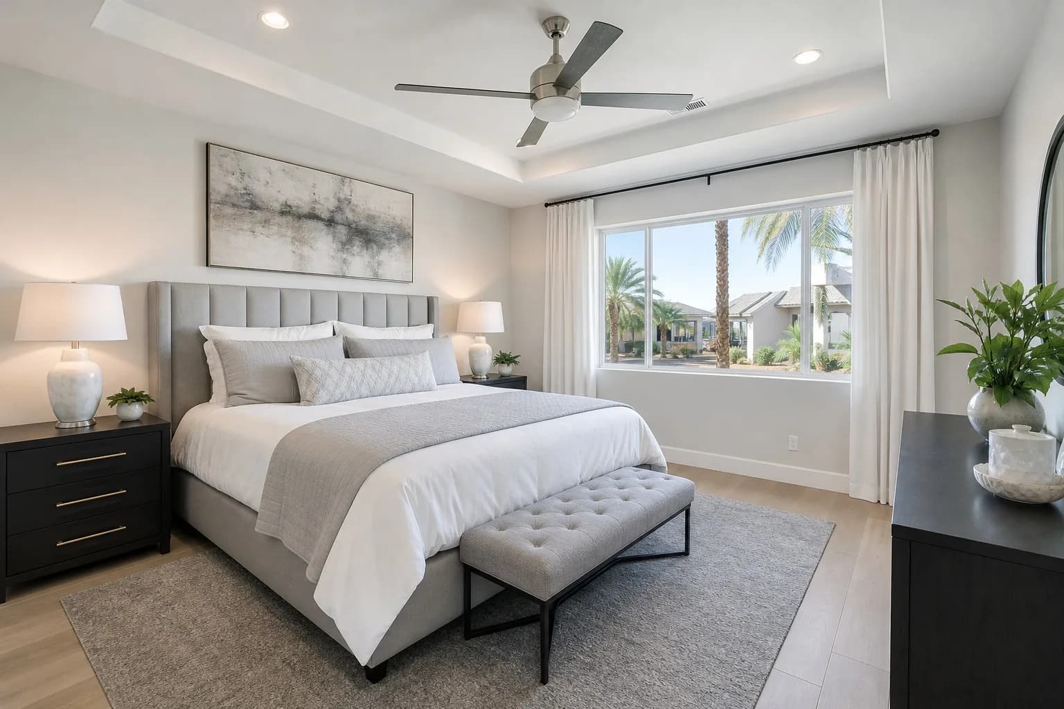 Spotlessly clean modern bedroom in a Las Vegas home with a neatly made bed, matching dark nightstands, ceiling fan, and large window with palm trees visible outside